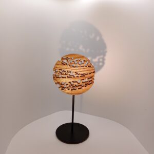 Sculpture Mini Forêt en bois d’orme ajouré, forme circulaire montée sur tige métallique et socle noir, projetant une ombre douce sur fond clair