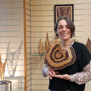 Corinne Bouloc, sculptrice sur bois - chantourneuse, dans sa boutique éphèmère à Espalion, en décembre 2025. Elle tient dans ses mains sa dernière oeuvre réalisée : Au fond de ton coeur.