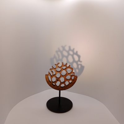 Sculpture miniature en bois de noyer ajouré, forme circulaire évoquant une canopée ou une forêt stylisée, montée sur une tige métallique noire avec socle rond, photographiée sur fond clair avec ombre porté