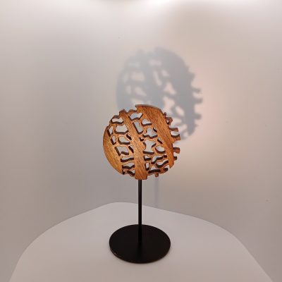 Sculpture Mini Forêt en bois de noyer ajouré, forme circulaire montée sur tige métallique et socle noir, projetant une ombre dense sur fond clair