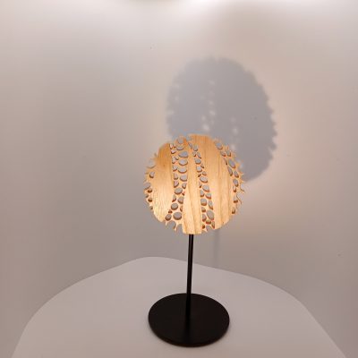 Sculpture Mini Forêt en bois de frêne ajouré, forme circulaire montée sur tige métallique et socle noir, projetant une ombre douce sur fond clair