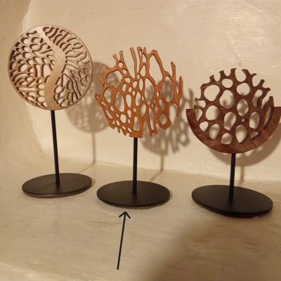 « Sculpture miniature en bois ajouré, formes organiques verticales évoquant une forêt stylisée ou des troncs entrelacés, montée sur une tige métallique noire avec socle rond »