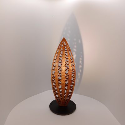 Sculpture miniature en bois de platane ajouré, forme verticale élancée évoquant une graine ou un tronc stylisé, montée sur socle noir.